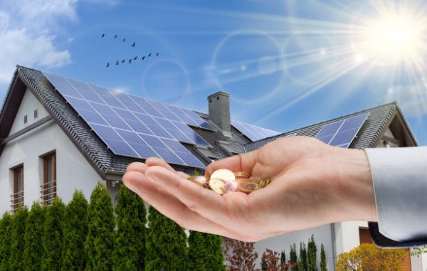 Una mano sosteniendo monedas frente a paneles solares, destacando qué debo considerar al instalar paneles solares en términos financieros