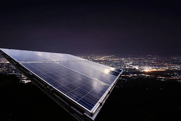 Conjunto de paneles solares y baterías iluminadas por luces cálidas, ejemplificando cómo los paneles solares generan electricidad de noche gracias al almacenamiento previo de energía.