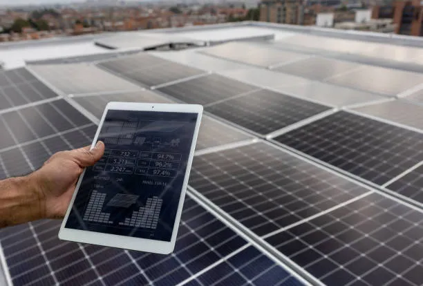 Ingeniero con casco y tablet junto a paneles solares sobre techo industrial, comprobando en tiempo real cómo sé cuánta energía están generando mis paneles solares.