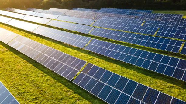 Filas de paneles solares instalados sobre pasto iluminados por un sol brillante que representa el aumento de demanda energética durante verano ¿Es normal que en verano el recibo sea más alto con paneles solares?