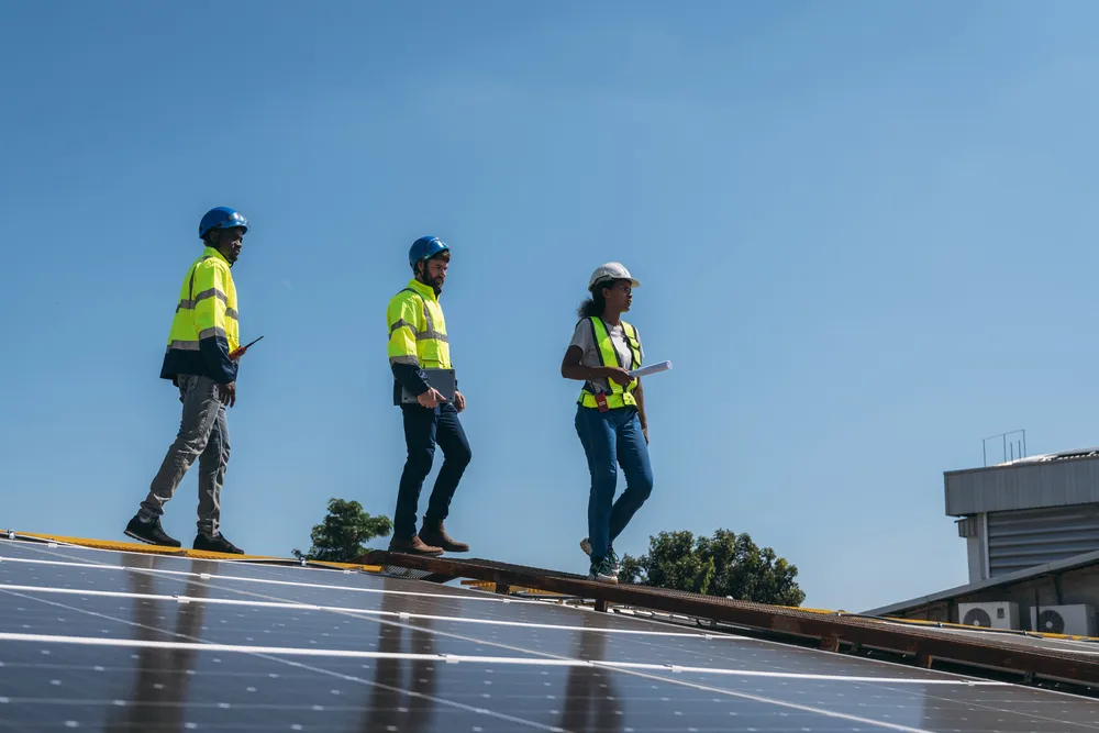 Supervisión experta durante el proceso de instalación de paneles solares: Tres profesionales en equipos de seguridad verifican la estructura y colocación de la matriz fotovoltaica en el techo.
