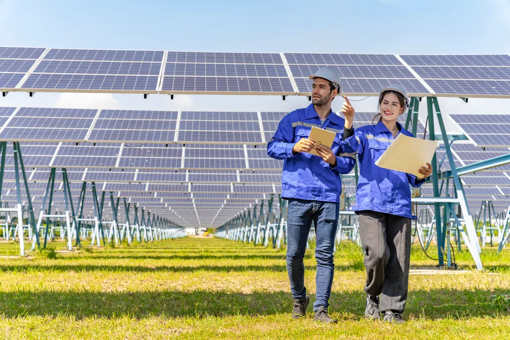Dos profesionales con uniforme azul y planos revisan el estado de las filas de módulos solares en una instalación a gran escala.