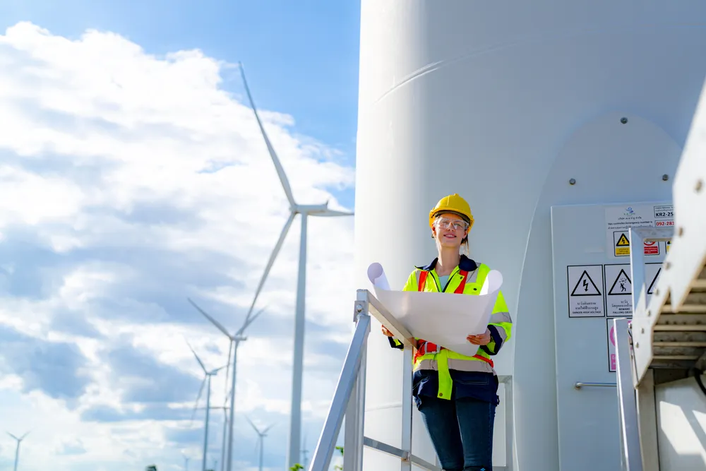 Una mujer ingeniera con casco de seguridad sostiene planos junto a una turbina eólica, simbolizando la apuesta por la energía limpia y la inclusión laboral dentro de los criterios ESG.