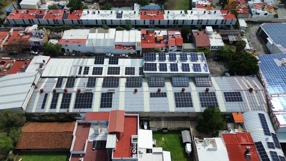 Vista aérea de un complejo industrial y casas con paneles solares instalados en sus techos bajo la luz del día clara.