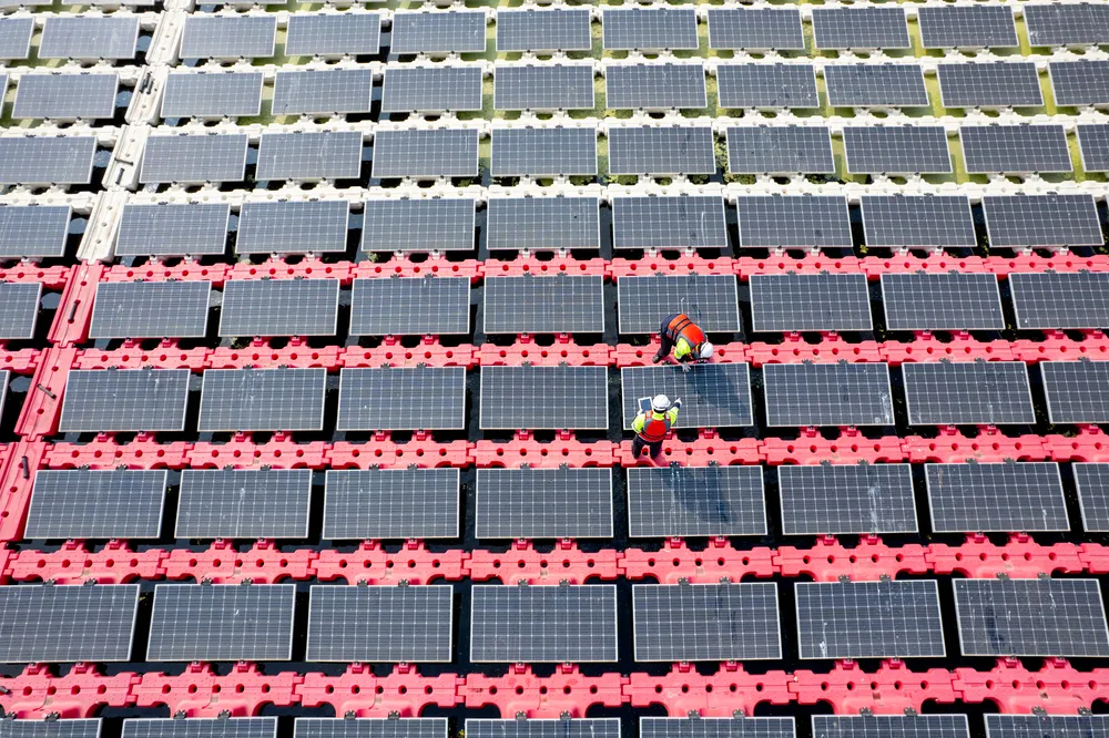 Dos técnicos con chalecos reflectantes revisan una tablet sobre paneles solares flotantes para reducir costos de energía.