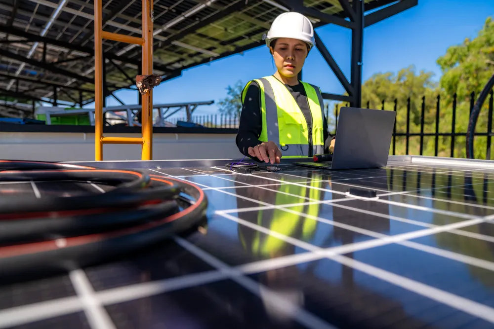 Ingeniera utiliza una laptop sobre un panel fotovoltaico para configurar el sistema de micro redes solares locales.