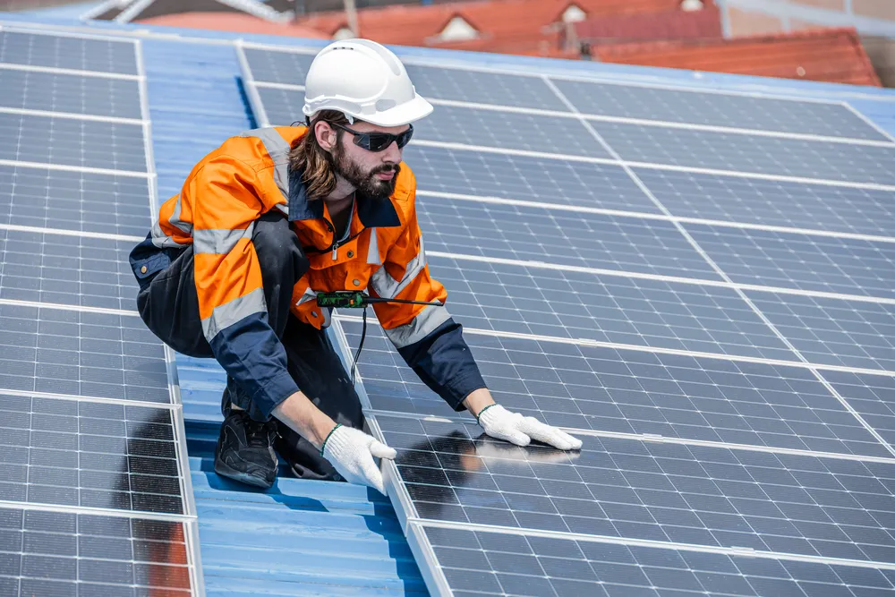 Trabajador con guantes y gafas de seguridad ajustando módulos durante el mantenimiento correctivo de paneles solares