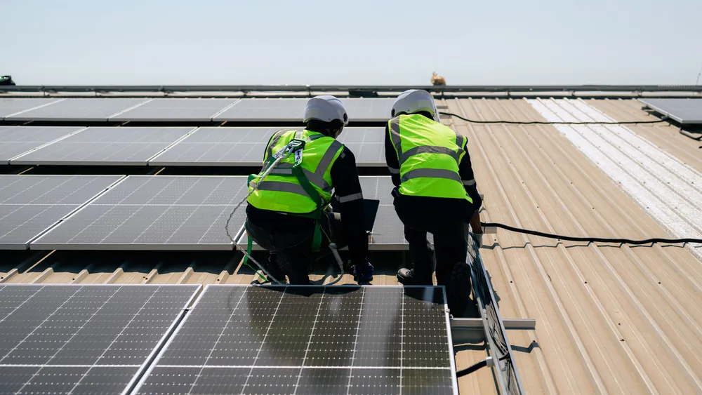 Dos operarios con chalecos de seguridad revisando el cableado y mantenimiento correctivo de paneles solares sobre el techo