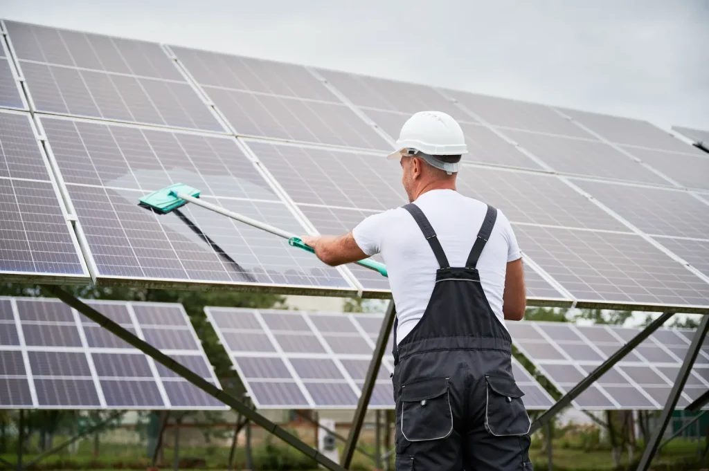 Cuánto cuesta un mantenimiento preventivo de paneles solares: Trabajador limpiando cuidadosamente una hilera de paneles