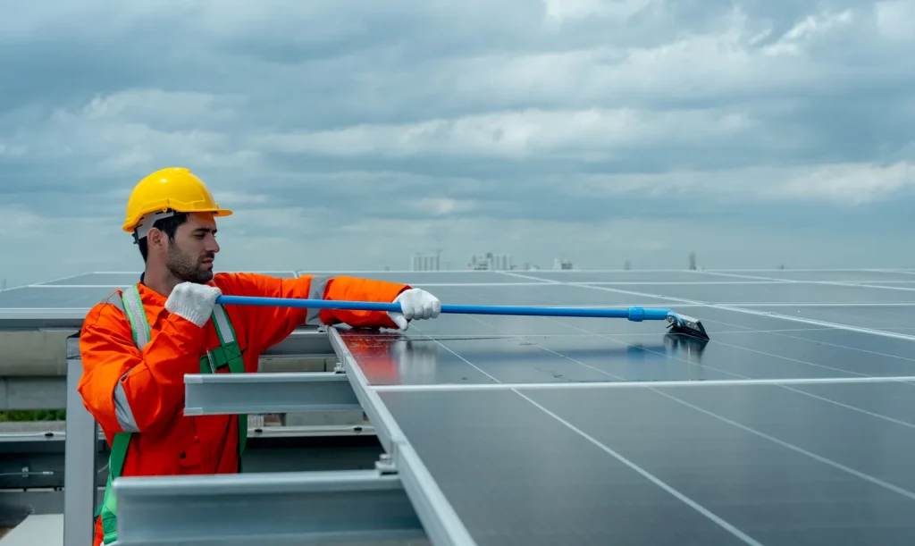 Cuánto cuesta un mantenimiento preventivo de paneles solares: Ingeniero limpiando paneles en una azotea urbana bajo un cielo nublado y denso.