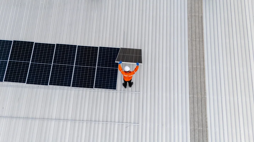 Técnico instalador colocando un módulo de paneles solares para fábricas y naves industriales sobre rieles de aluminio.
