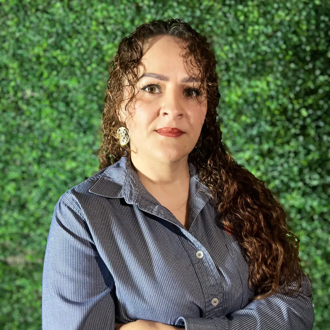 Byanca García, del equipo de administración de una empresa de paneles solares, posando ante un muro verde.