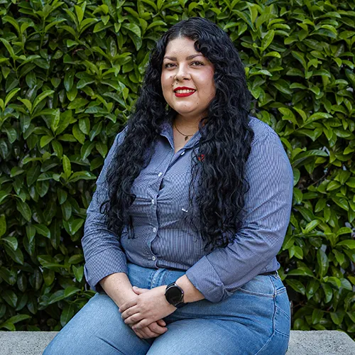 Jeanette Rodríguez, responsable de Recursos Humanos en una empresa de paneles solares, sentada frente a un follaje natural.