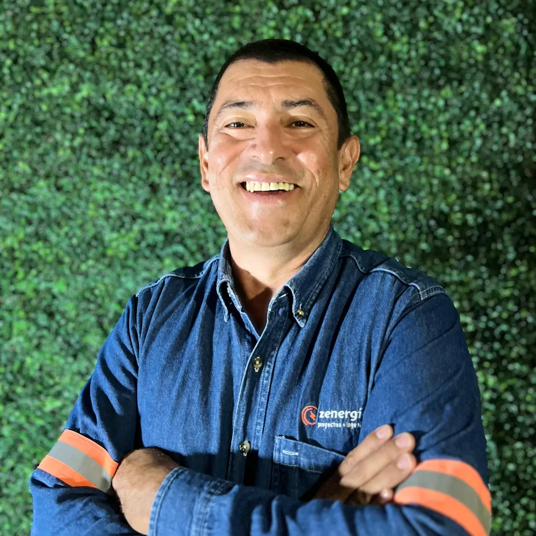 José Luis, gerente operativo de una empresa de paneles solares, con uniforme de trabajo y brazos cruzados frente a un muro verde.