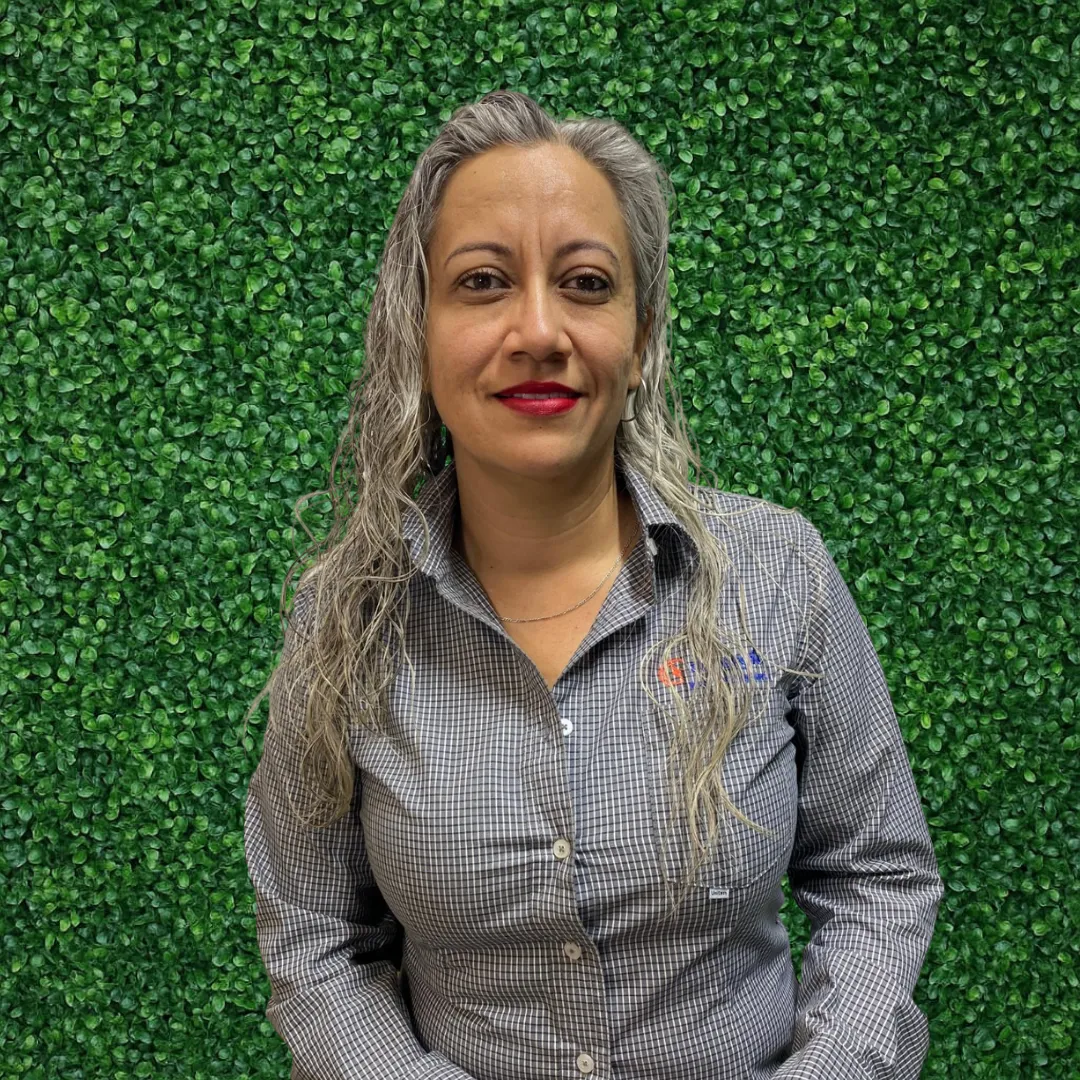 Martha Velázquez, especialista en telemarketing para una empresa de paneles solares, posando con una sonrisa ante un muro verde.