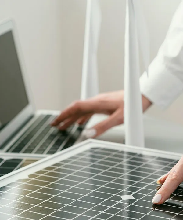 Manos trabajando con laptop y tocando un panel solar para calcular el ahorro o financiamiento.