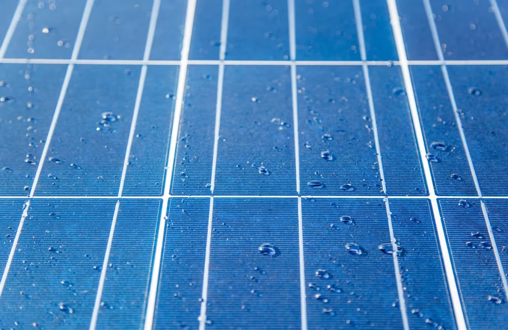 Gotas de agua sobre un sistema de paneles solares fotovoltaicos azules, mostrando de cerca sus celdas de silicio.