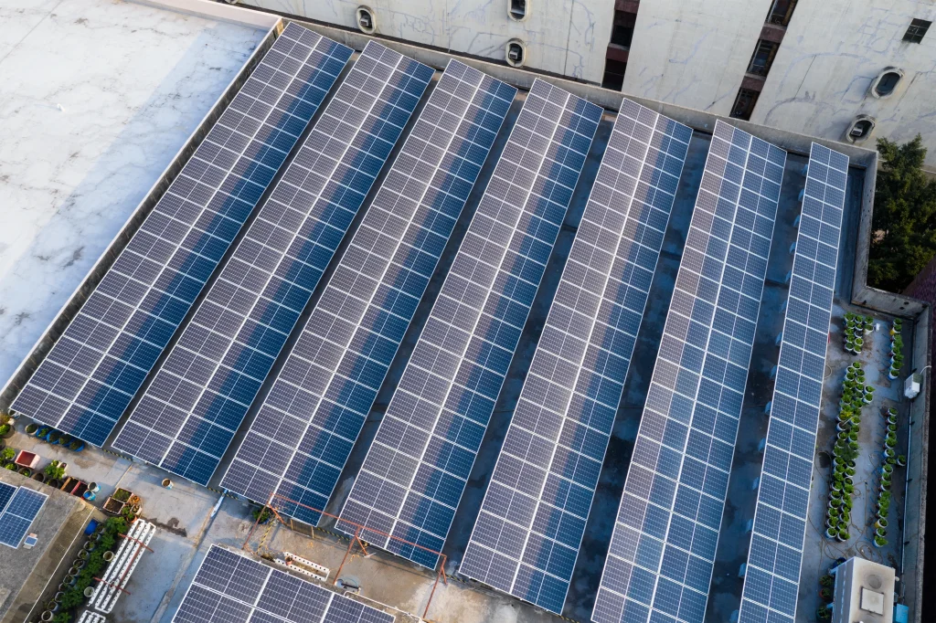 Una gran instalación de paneles solares fotovoltaicos cubre el techo de un edificio industrial, con filas de paneles alineados en ángulo para maximizar la exposición al sol.